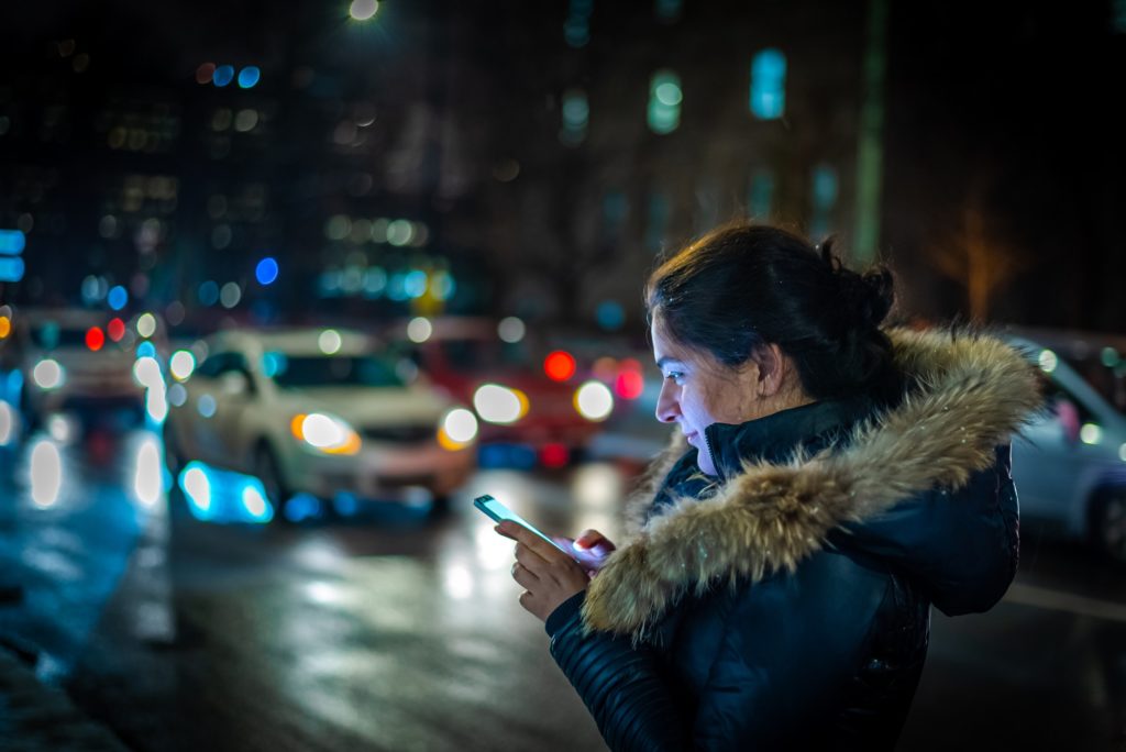 Girl booking online taxi cab uber at night in city street